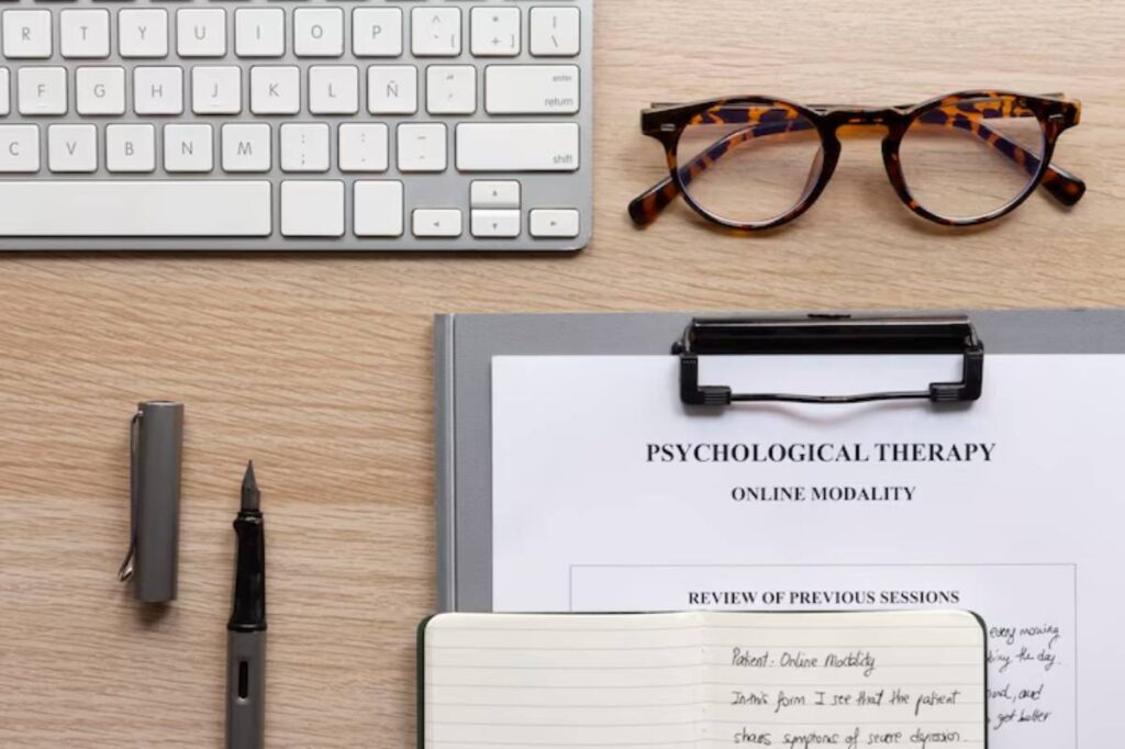 A workspace with a keyboard, tortoiseshell glasses, a notebook, and documents about online psychological therapy.