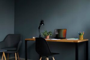 A stylish home office featuring a wooden desk with a laptop, a desk lamp, a plant, and colorful stationery in a cozy corner.