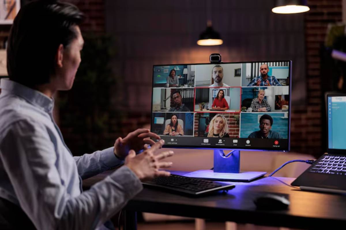 A person engages in a video conference on a large monitor, showcasing multiple participants in a modern workspace. 