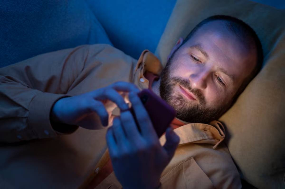 A man lying down indoors, comfortably resting with his hands on his phone. 