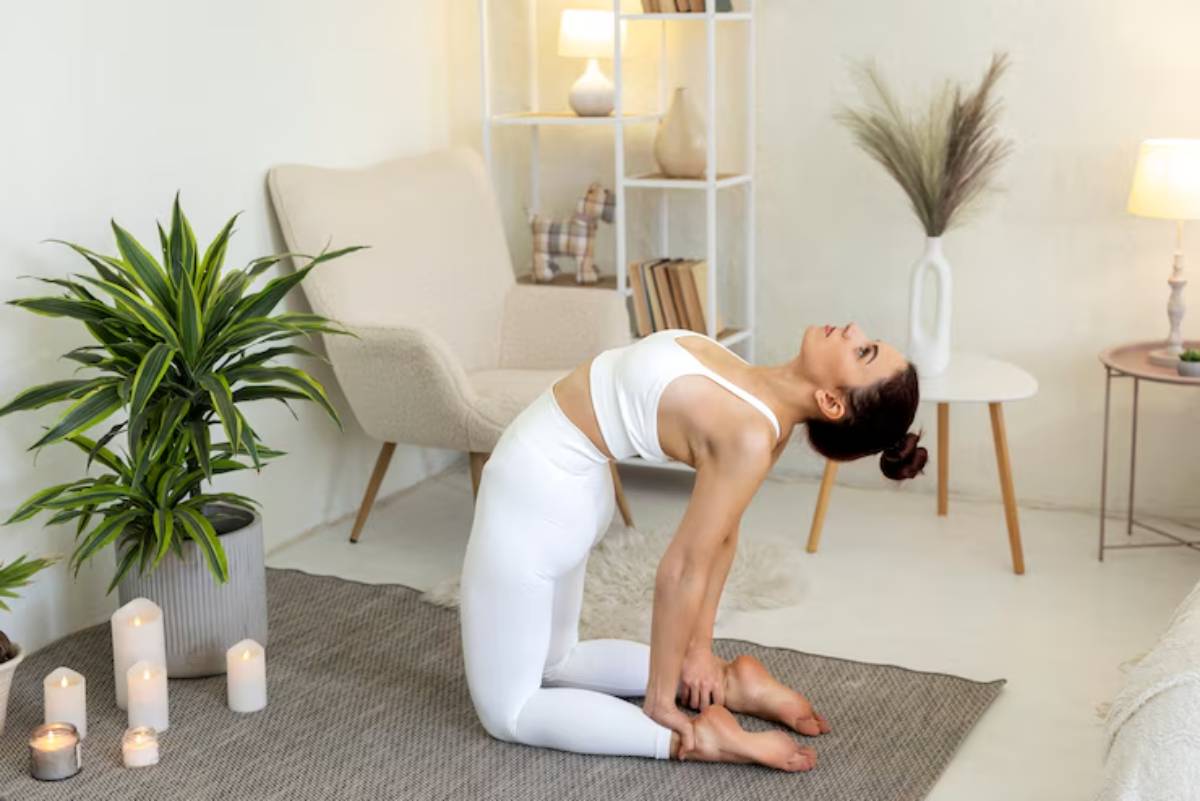  A person in white activewear performs a yoga pose on a rug surrounded by candles and plants in a cozy, minimalist room.