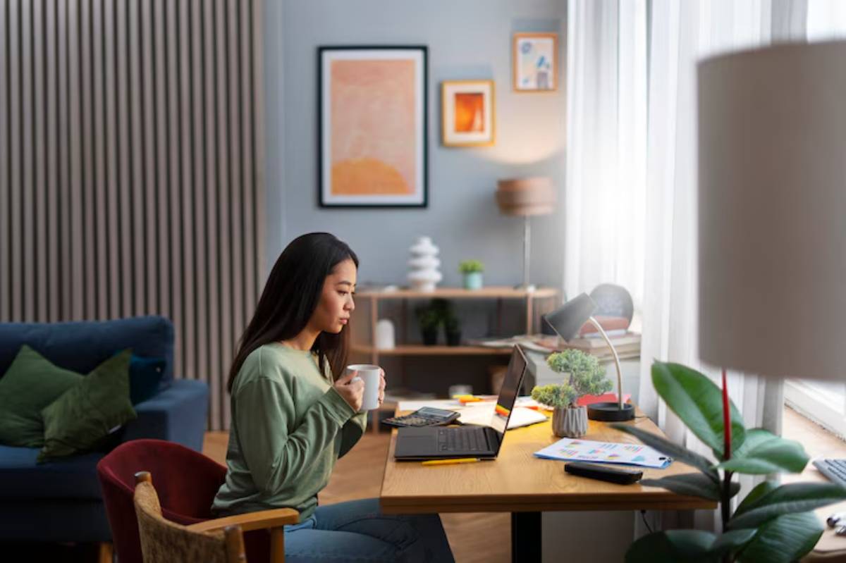 A cozy home office setup with a person holding a mug, sitting at a desk with a laptop, surrounded by plants and decorative items. 