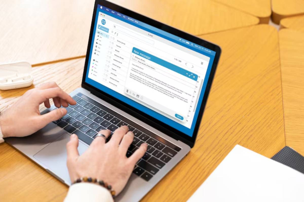 A person typing on a laptop displaying an email interface, surrounded by modern office furniture and stationery. 